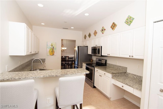 kitchen featuring appliances with stainless steel finishes, white cabinets, a peninsula, and a kitchen bar