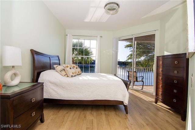 bedroom with light wood finished floors, a water view, and access to exterior