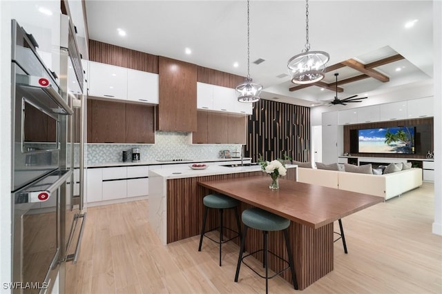 kitchen with a kitchen island with sink, hanging light fixtures, white cabinetry, and coffered ceiling