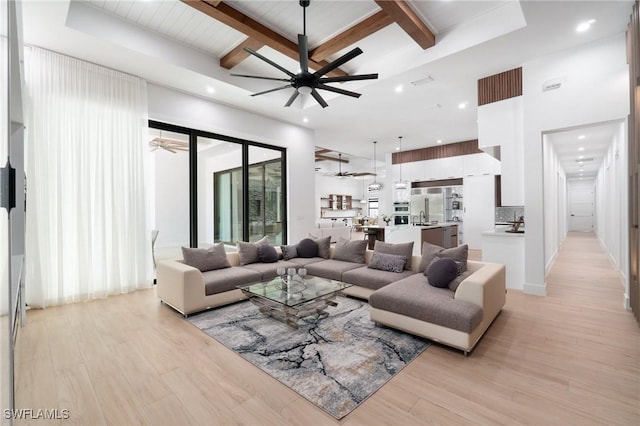 living room featuring ceiling fan, beam ceiling, a towering ceiling, coffered ceiling, and light wood-type flooring