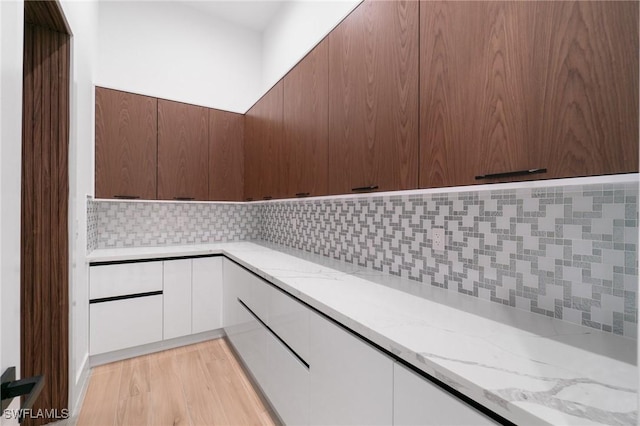 interior space featuring light hardwood / wood-style flooring, light stone countertops, decorative backsplash, and white cabinets