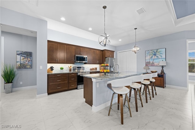 142 SW 35th Ave, Cape Coral, FL 33991 - kitchen featuring decorative light fixtures, a center island with sink, a kitchen breakfast bar, stainless steel appliances, and light stone countertops