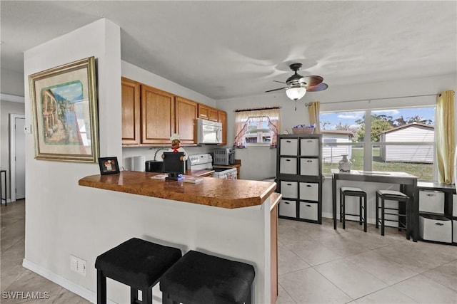 kitchen with light tile patterned flooring, a kitchen breakfast bar, ceiling fan, kitchen peninsula, and electric stove