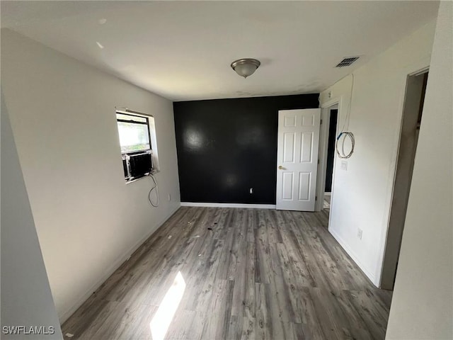 unfurnished bedroom with cooling unit, visible vents, baseboards, and wood finished floors