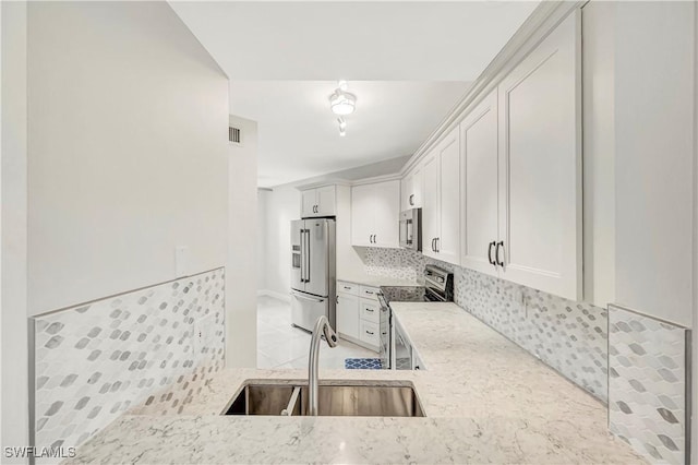 kitchen with appliances with stainless steel finishes, sink, white cabinets, and light stone counters