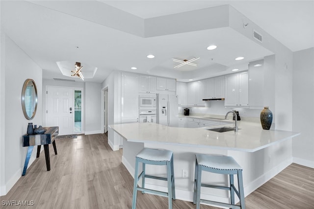 kitchen featuring white cabinetry, white appliances, a kitchen breakfast bar, and kitchen peninsula