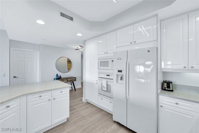 kitchen featuring white cabinetry, light stone countertops, light wood-type flooring, and white appliances