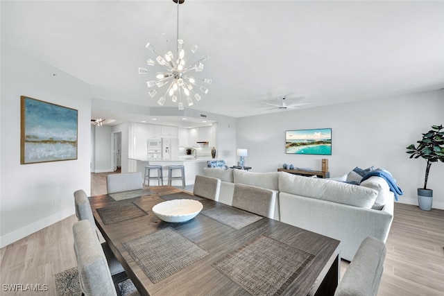 dining space with ceiling fan with notable chandelier and light hardwood / wood-style flooring