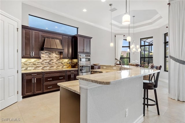 kitchen featuring a breakfast bar area, a spacious island, custom range hood, decorative light fixtures, and stainless steel double oven