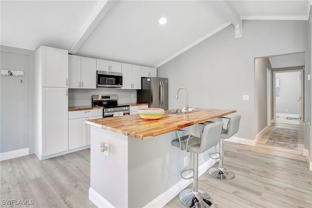 kitchen with butcher block countertops, white cabinetry, a kitchen breakfast bar, stainless steel appliances, and an island with sink