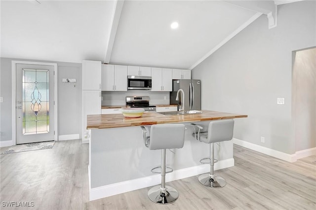 kitchen featuring appliances with stainless steel finishes, butcher block countertops, a breakfast bar area, white cabinets, and a center island with sink