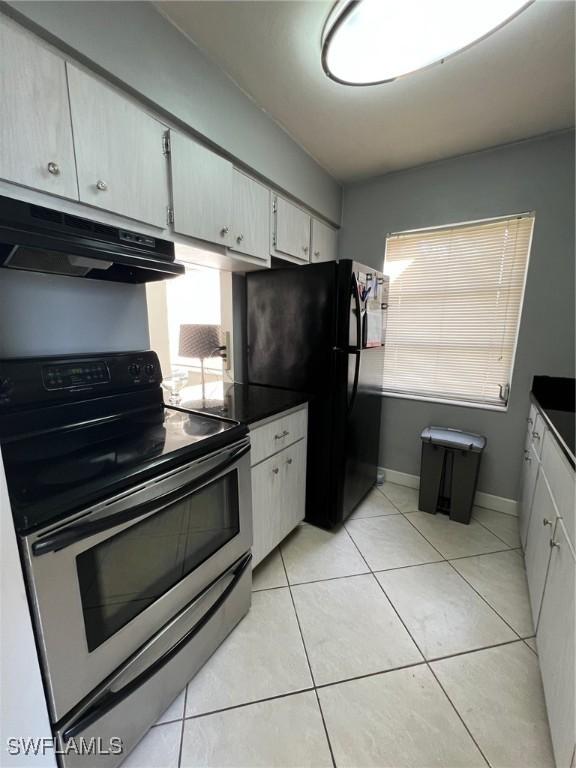 kitchen with black refrigerator, light tile patterned floors, white cabinetry, and stainless steel electric stove