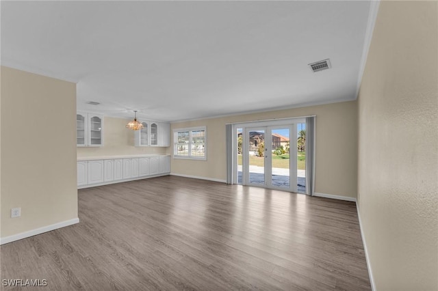 unfurnished living room with hardwood / wood-style flooring, crown molding, and a notable chandelier