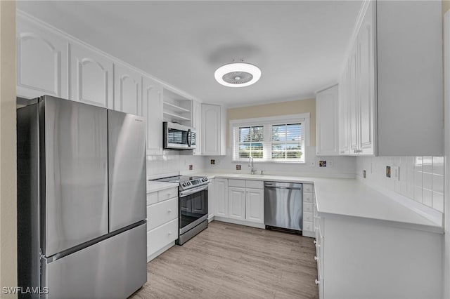 kitchen featuring appliances with stainless steel finishes, tasteful backsplash, sink, white cabinets, and light hardwood / wood-style flooring