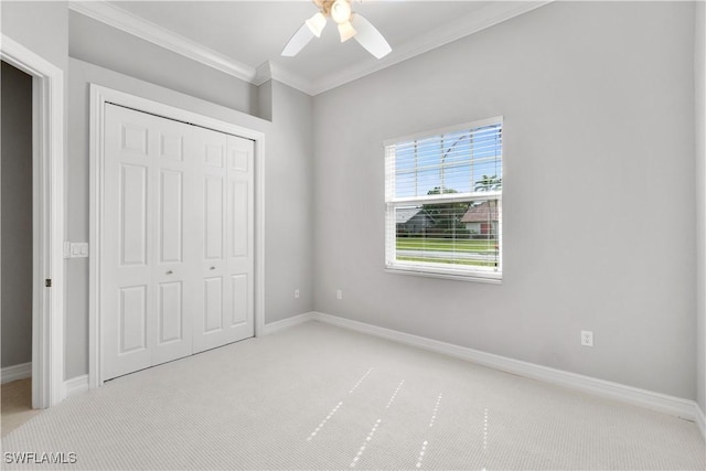 unfurnished bedroom with light colored carpet, crown molding, a ceiling fan, baseboards, and a closet