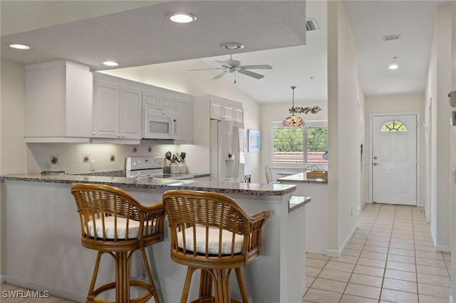 kitchen featuring a kitchen breakfast bar, kitchen peninsula, stone counters, white appliances, and white cabinets