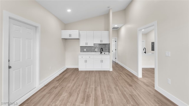 kitchen with vaulted ceiling, white cabinetry, sink, decorative backsplash, and light wood-type flooring