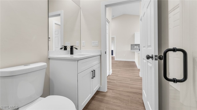 bathroom featuring vanity, wood-type flooring, toilet, and vaulted ceiling