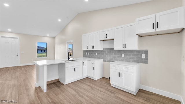 kitchen with sink, white cabinetry, backsplash, kitchen peninsula, and light wood-type flooring