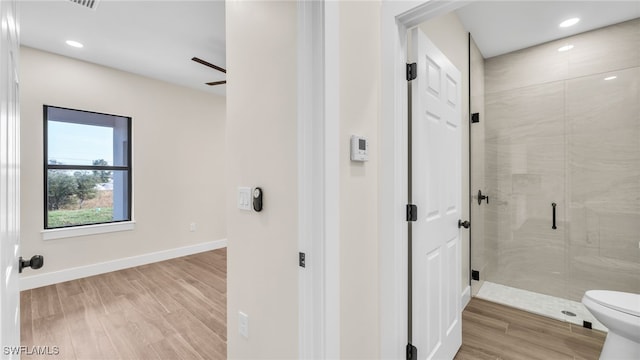 bathroom with ceiling fan, hardwood / wood-style flooring, a shower with door, and toilet