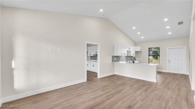 interior space with high vaulted ceiling, white cabinetry, backsplash, kitchen peninsula, and light wood-type flooring