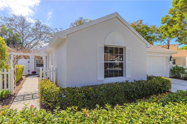 view of side of property featuring an attached garage, fence, and stucco siding