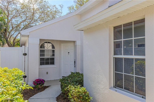 view of exterior entry with fence and stucco siding