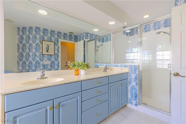 bathroom with wallpapered walls, a shower stall, double vanity, and a sink