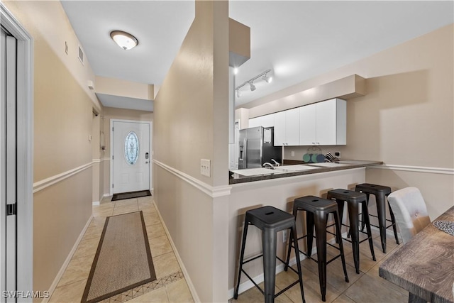 kitchen with a breakfast bar, white cabinetry, stainless steel refrigerator with ice dispenser, light tile patterned flooring, and kitchen peninsula