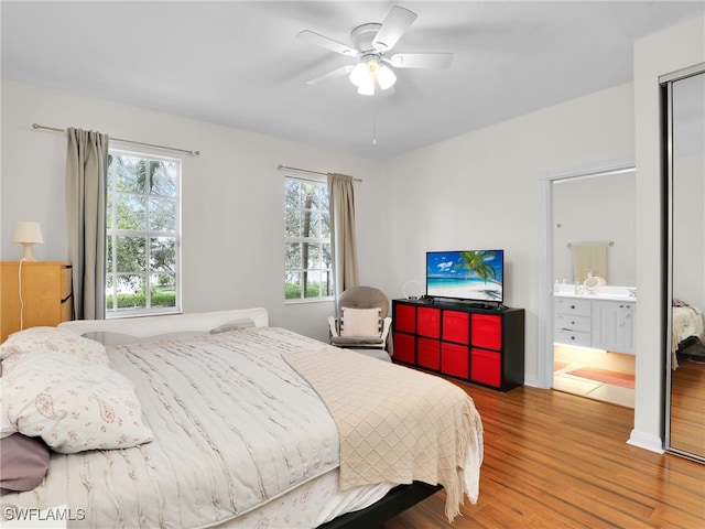 bedroom featuring a ceiling fan, multiple windows, ensuite bath, and wood finished floors