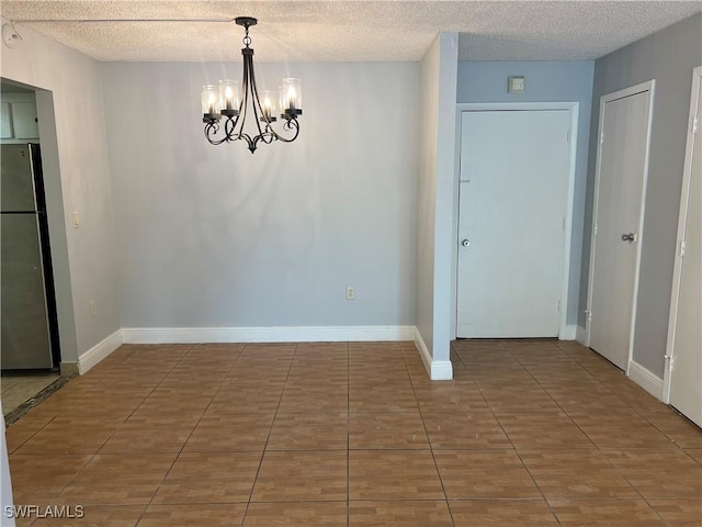 tiled empty room featuring a notable chandelier and a textured ceiling