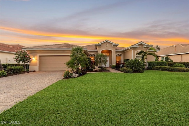 mediterranean / spanish-style home featuring a garage, a tiled roof, decorative driveway, a front lawn, and stucco siding