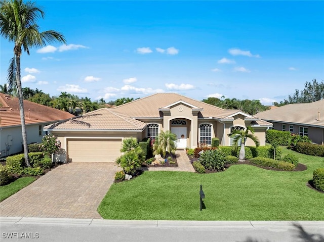 mediterranean / spanish-style home featuring a tiled roof, an attached garage, decorative driveway, a front yard, and stucco siding