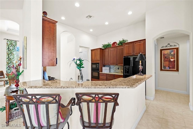 kitchen with arched walkways, a peninsula, black appliances, and a breakfast bar area