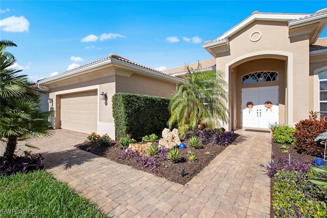 view of exterior entry featuring a tiled roof, decorative driveway, an attached garage, and stucco siding