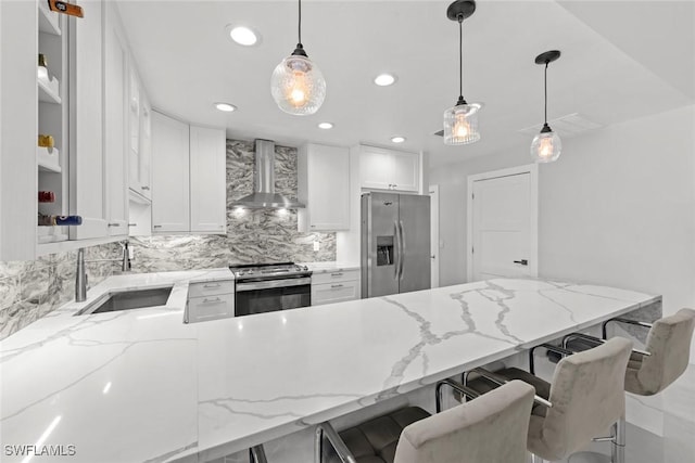 kitchen featuring a breakfast bar, a sink, wall chimney range hood, appliances with stainless steel finishes, and open shelves