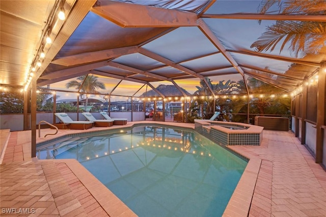 pool at dusk featuring an in ground hot tub, a patio area, glass enclosure, and an outdoor pool