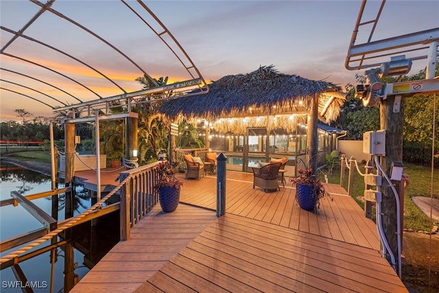 deck at dusk with a dock, a water view, boat lift, and an outdoor pool