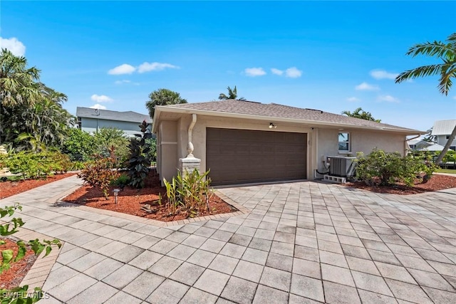 ranch-style home with a garage, decorative driveway, cooling unit, and stucco siding