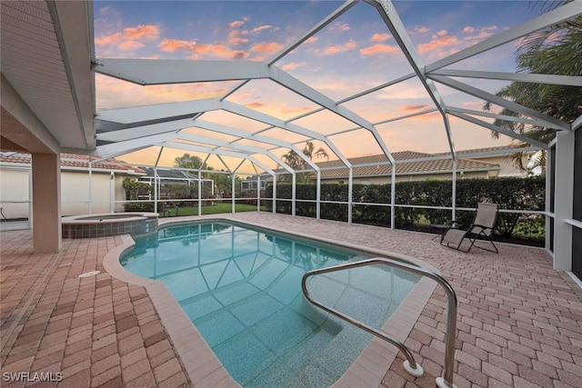 pool at dusk featuring a pool with connected hot tub, a patio area, and a lanai