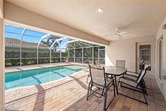 view of swimming pool with glass enclosure, ceiling fan, a fenced in pool, and a patio