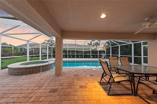 pool at dusk with ceiling fan, a patio, and glass enclosure