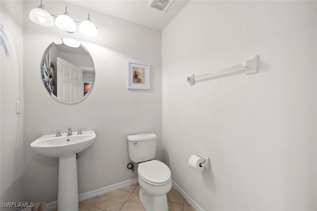 half bath featuring baseboards, visible vents, toilet, tile patterned floors, and a sink