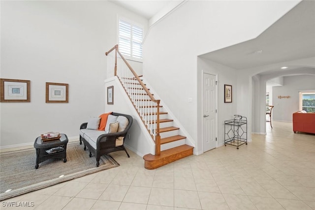 stairs with arched walkways, a high ceiling, tile patterned flooring, and baseboards