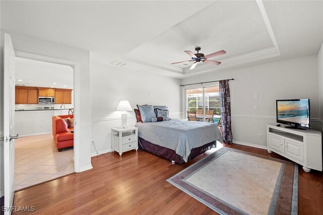 bedroom with baseboards, ceiling fan, wood finished floors, access to exterior, and a tray ceiling