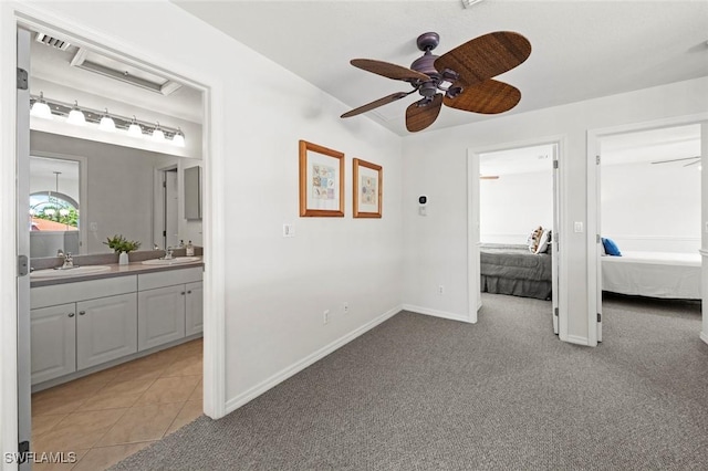 bedroom featuring light tile patterned floors, ensuite bathroom, a sink, and light colored carpet