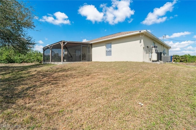 rear view of house with a sunroom, a lawn, central AC unit, and stucco siding