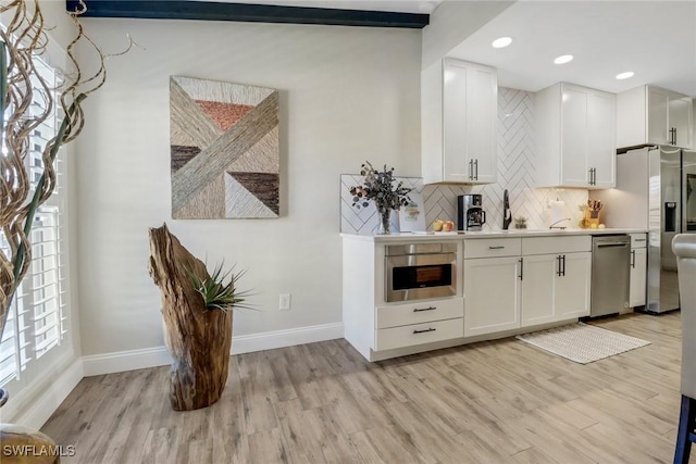 bar featuring tasteful backsplash, stainless steel appliances, light hardwood / wood-style flooring, and white cabinets