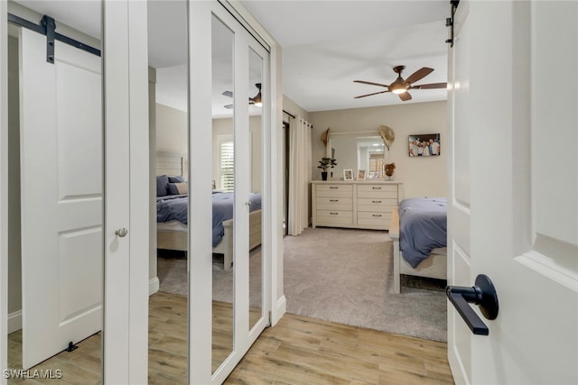 bedroom with light hardwood / wood-style flooring, a barn door, and ceiling fan