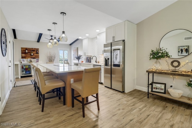 kitchen featuring white cabinets, hanging light fixtures, a center island, stainless steel appliances, and light wood-type flooring